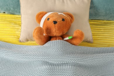 Photo of Cute teddy bear with bandage and thermometer on bed, top view