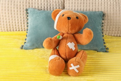 Photo of Cute teddy bear with bandages, adhesive medical plasters and thermometer on bed