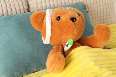 Photo of Cute teddy bear with bandages, adhesive medical plasters and thermometer on bed