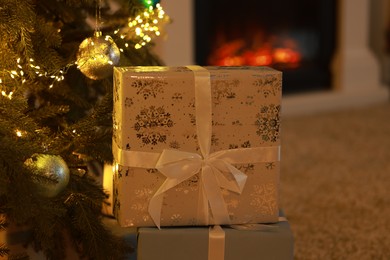 Photo of Gift boxes under Christmas tree near fireplace indoors