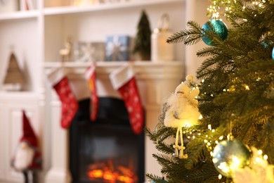 Photo of Christmas tree with baubles near fireplace indoors, closeup