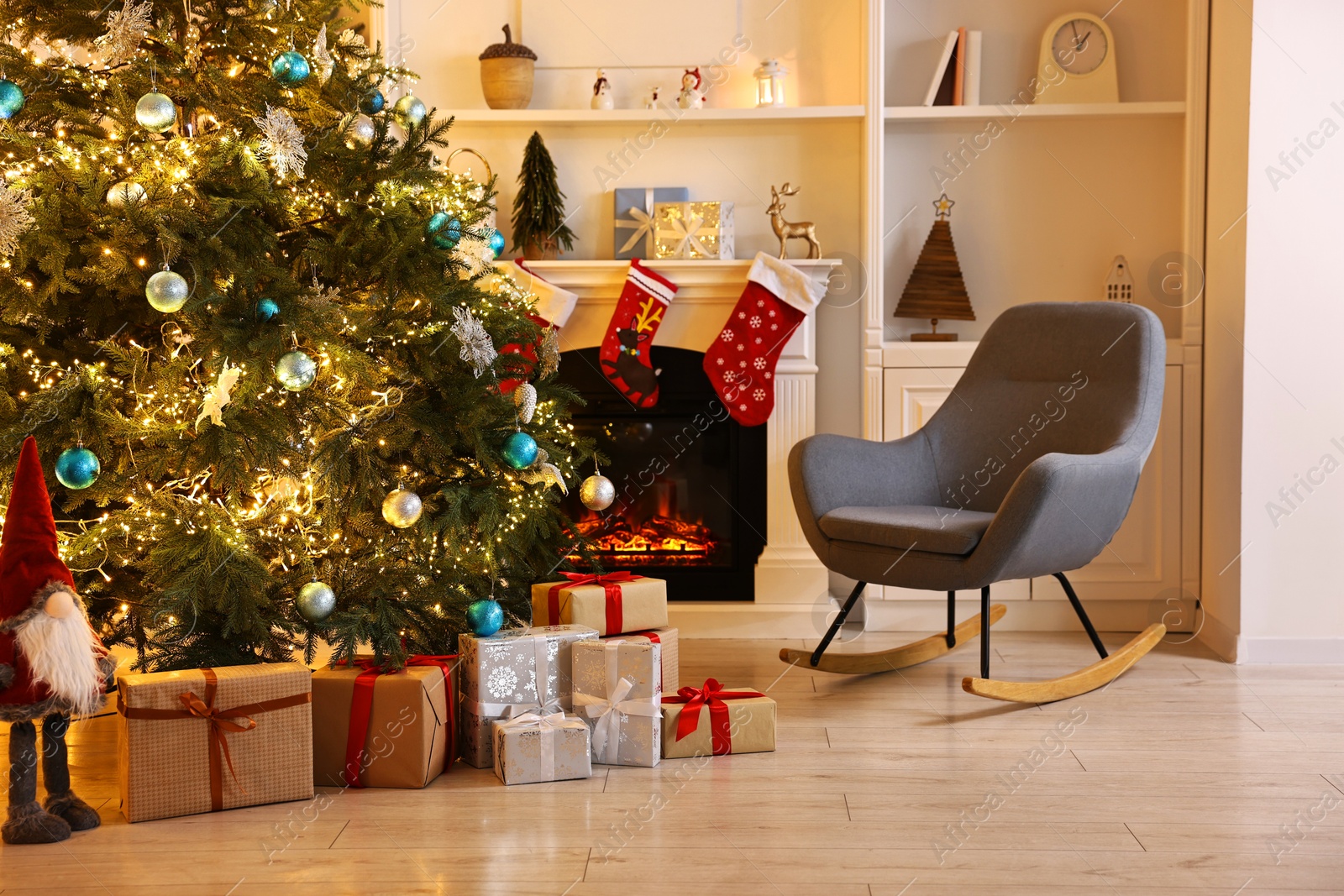 Photo of Christmas tree and rocking chair near decorated fireplace in room. Festive interior