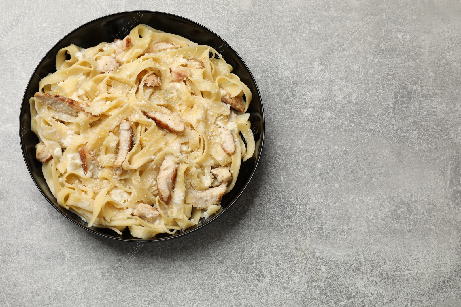 Photo of Tasty Alfredo pasta with chicken on light grey table, top view. Space for text