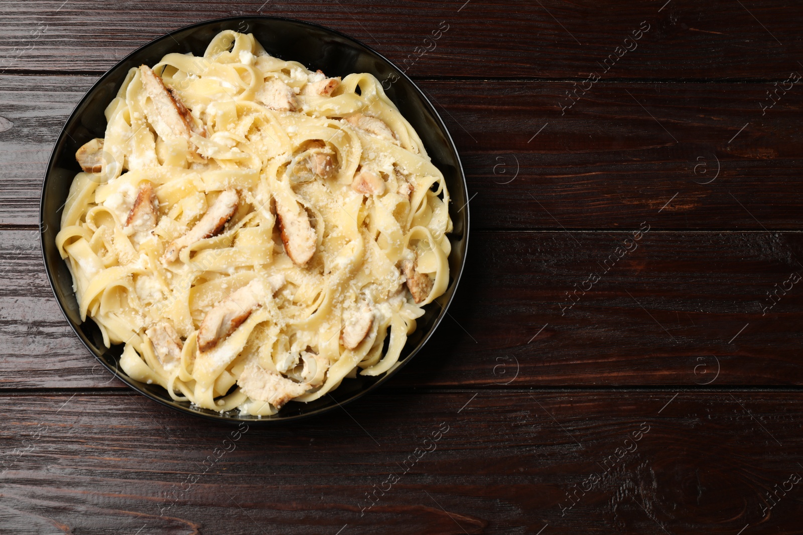 Photo of Tasty Alfredo pasta with chicken on wooden table, top view. Space for text