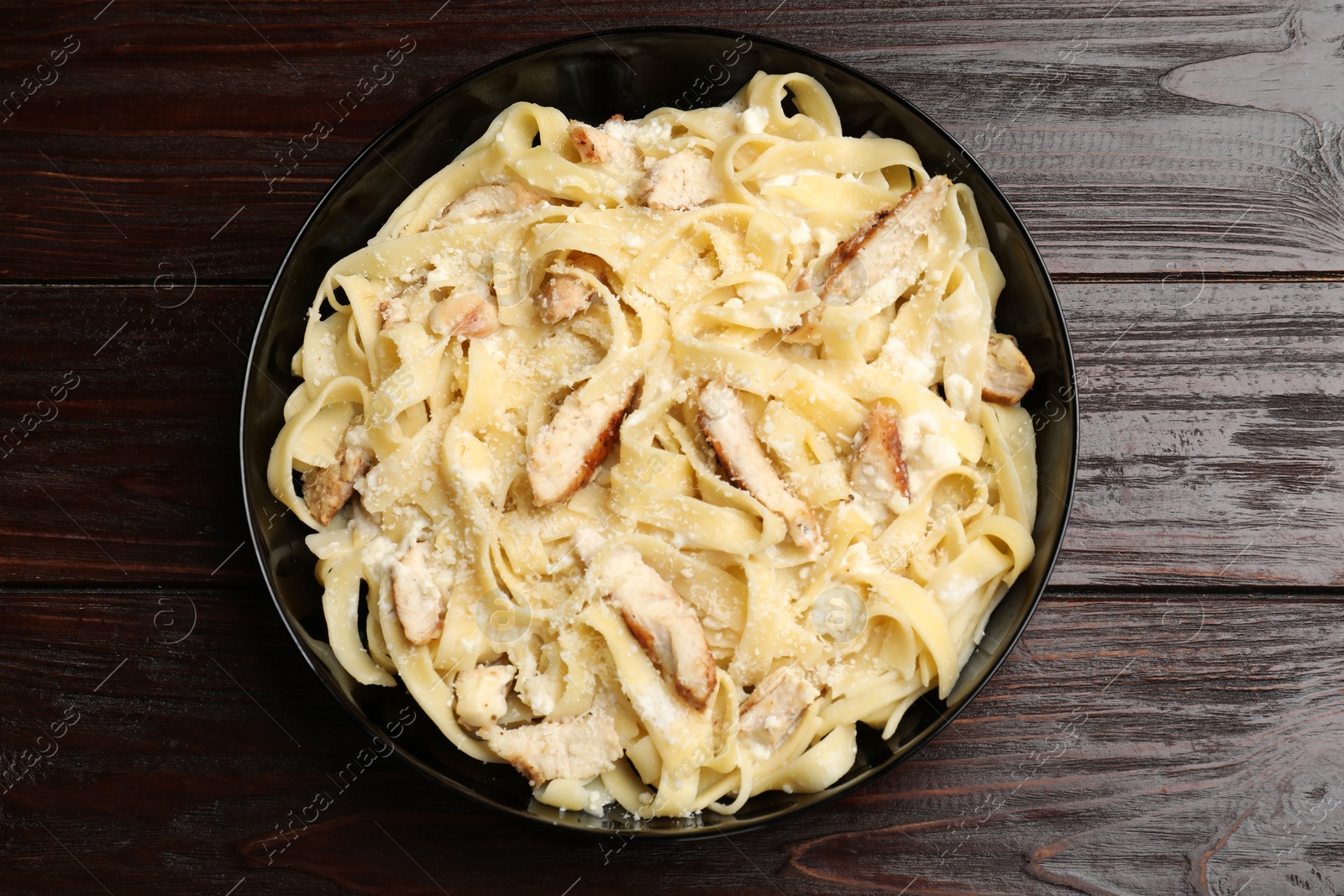 Photo of Tasty Alfredo pasta with chicken on wooden table, top view