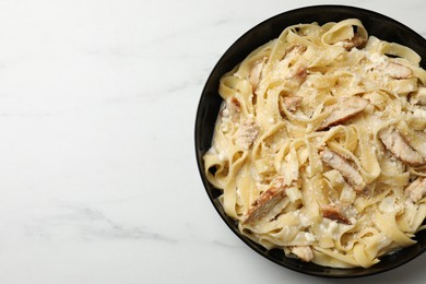 Photo of Tasty Alfredo pasta with chicken on white marble table, top view. Space for text