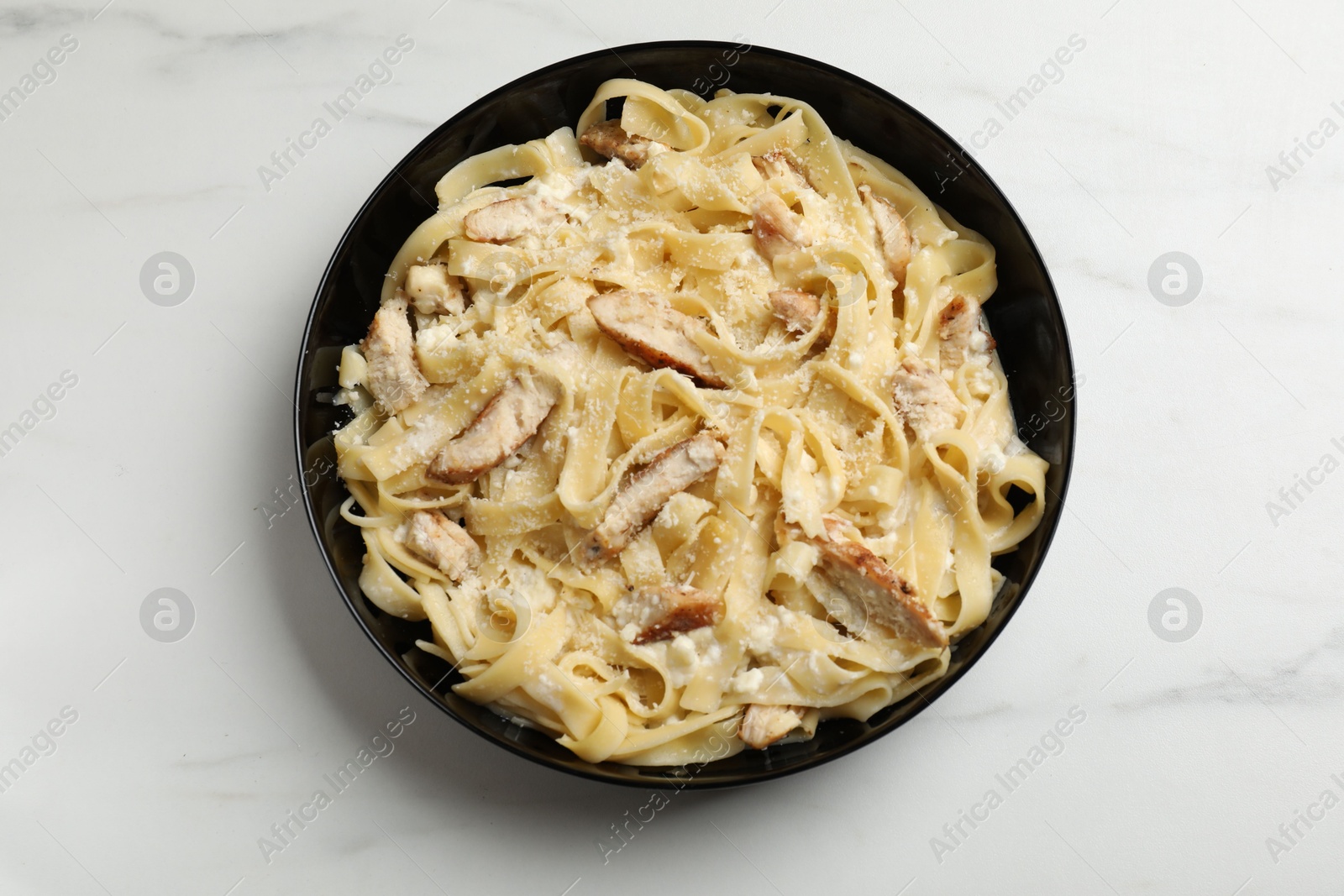 Photo of Tasty Alfredo pasta with chicken on white marble table, top view