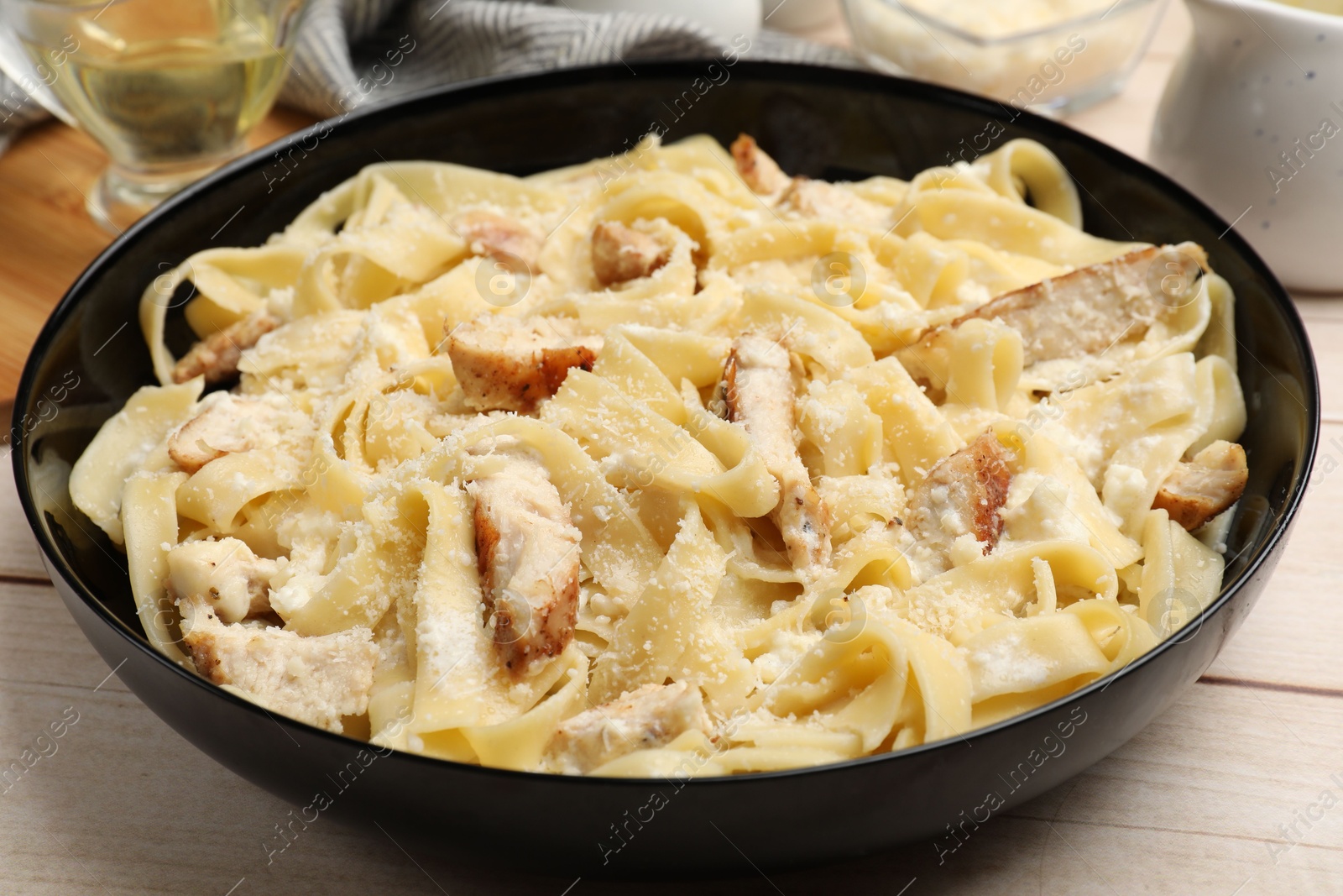 Photo of Tasty Alfredo pasta with chicken on light wooden table, closeup