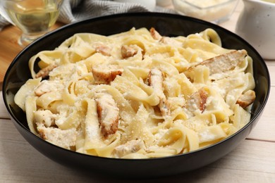 Photo of Tasty Alfredo pasta with chicken on light wooden table, closeup