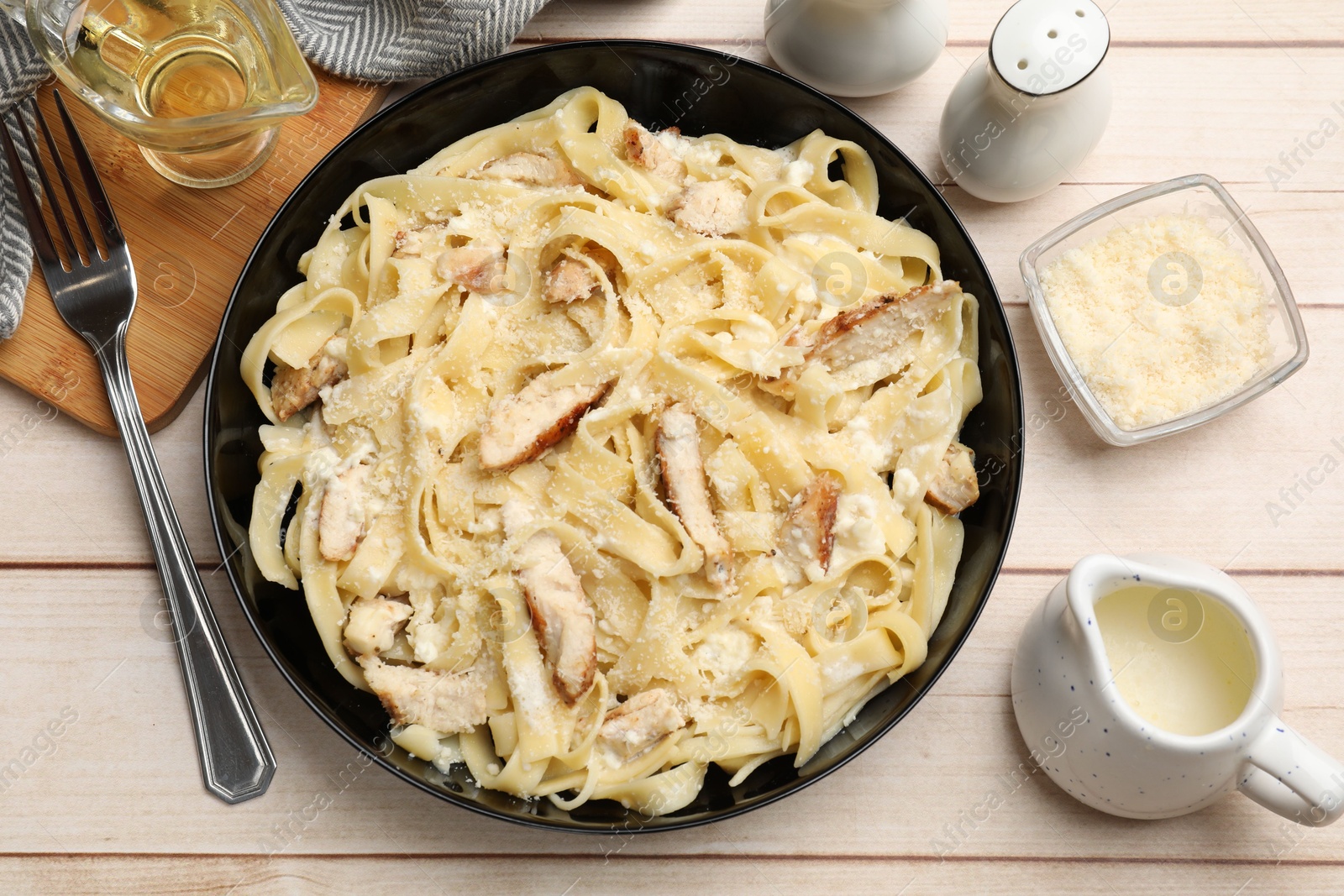 Photo of Tasty Alfredo pasta with chicken served on light wooden table, flat lay