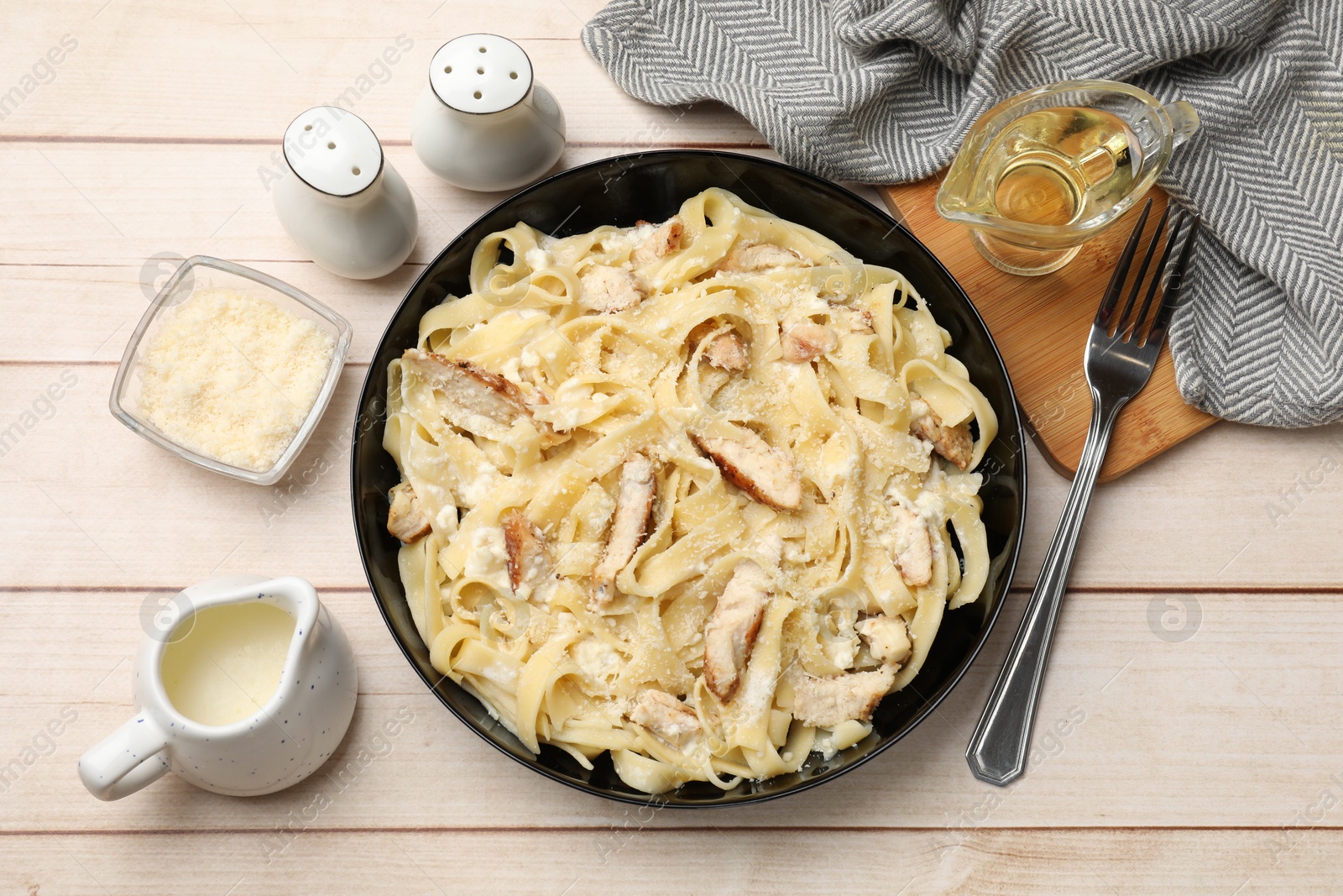 Photo of Tasty Alfredo pasta with chicken served on light wooden table, flat lay