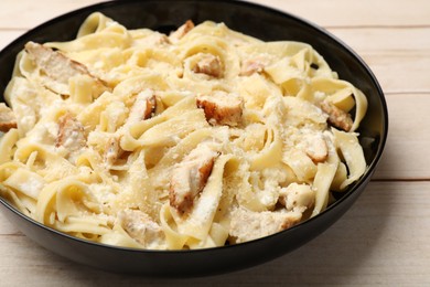 Photo of Tasty Alfredo pasta with chicken on light wooden table, closeup