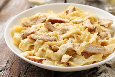 Photo of Tasty Alfredo pasta with chicken on wooden table, closeup