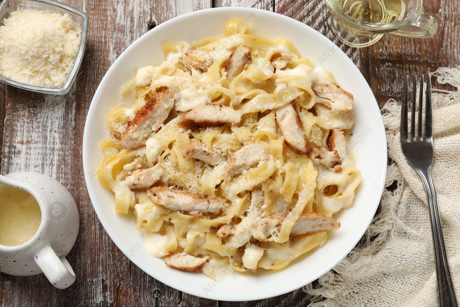 Photo of Tasty Alfredo pasta with chicken served on wooden table, flat lay