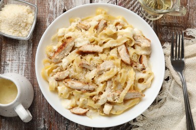 Photo of Tasty Alfredo pasta with chicken served on wooden table, flat lay