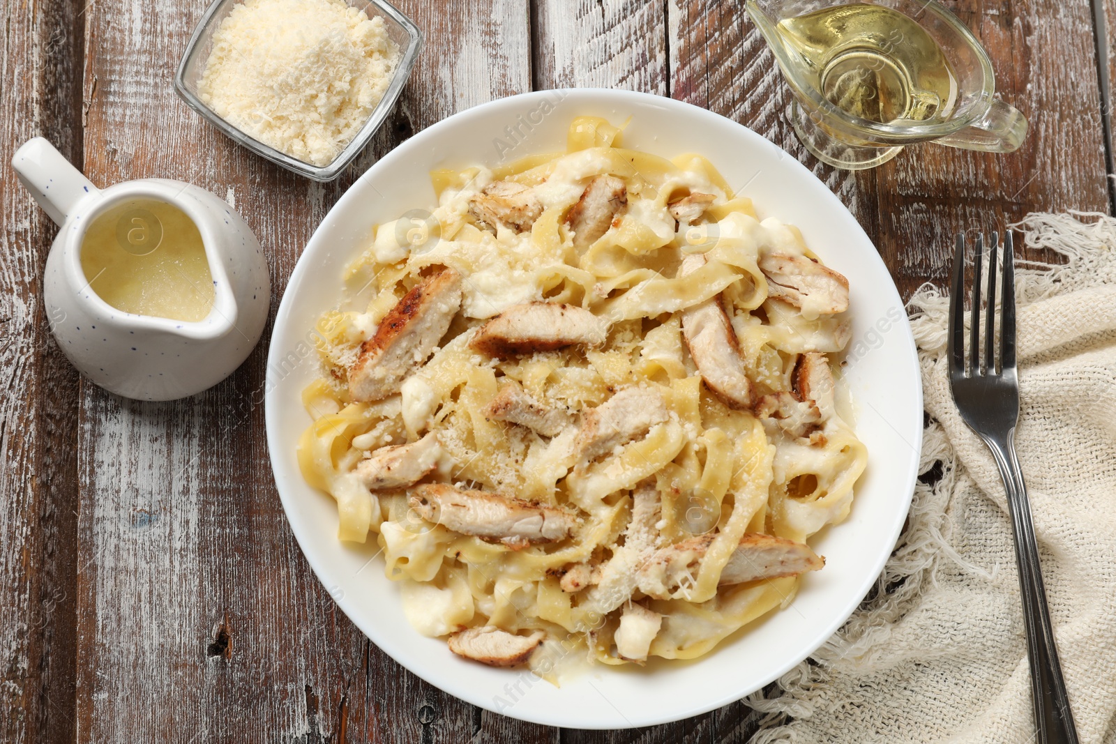 Photo of Tasty Alfredo pasta with chicken served on wooden table, flat lay