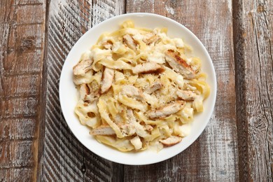 Photo of Tasty Alfredo pasta with chicken on wooden table, top view