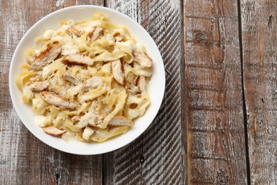 Photo of Tasty Alfredo pasta with chicken on wooden table, top view. Space for text