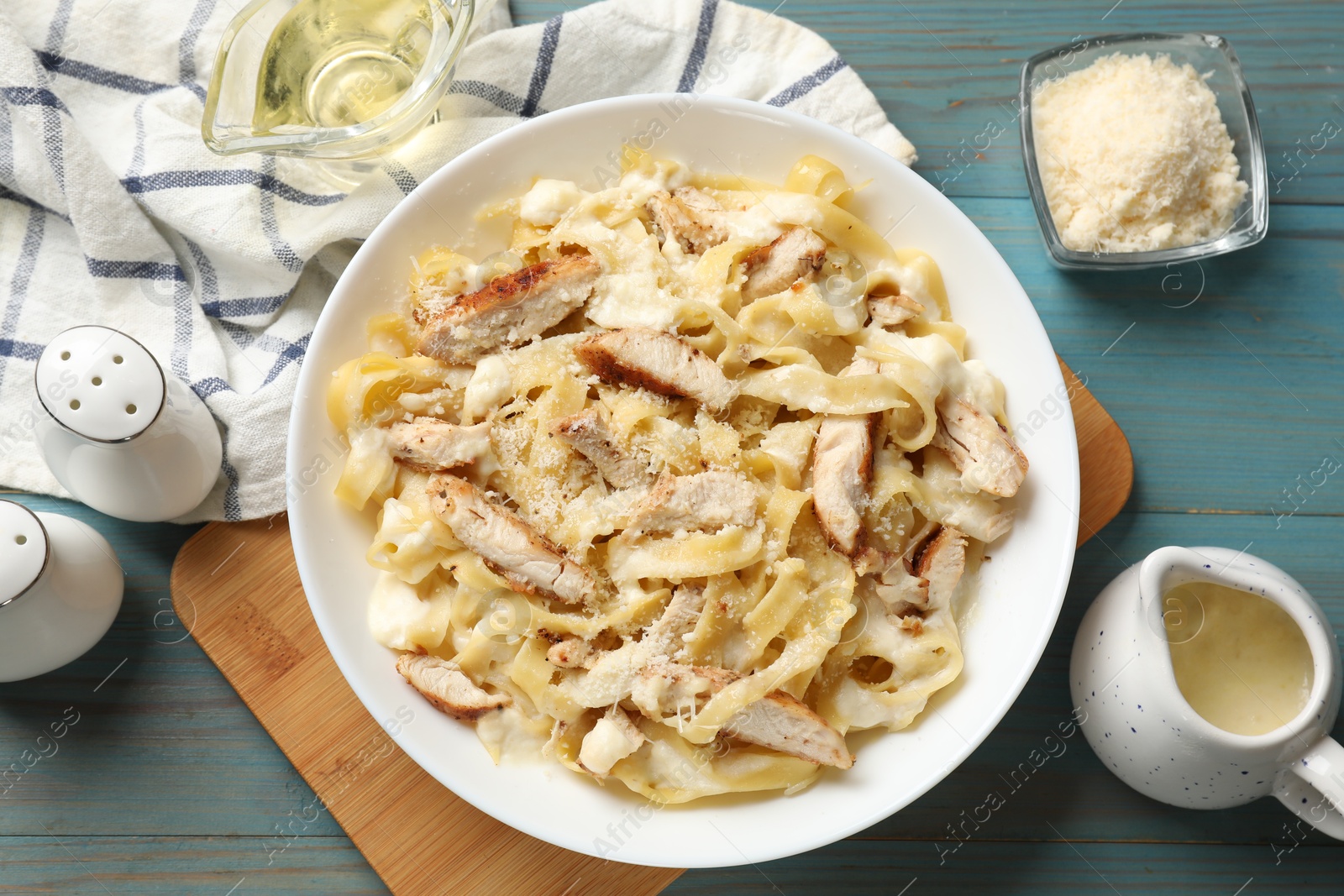 Photo of Tasty Alfredo pasta with chicken on light blue wooden table, flat lay