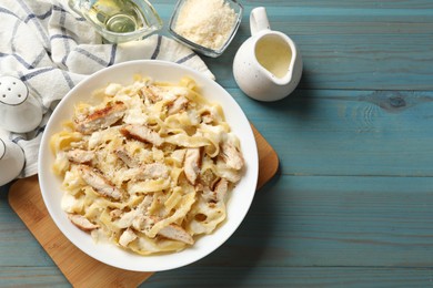 Photo of Tasty Alfredo pasta with chicken on light blue wooden table, flat lay. Space for text