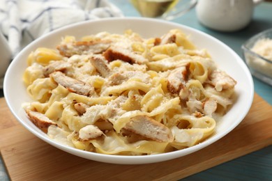 Photo of Tasty Alfredo pasta with chicken on light blue wooden table, closeup