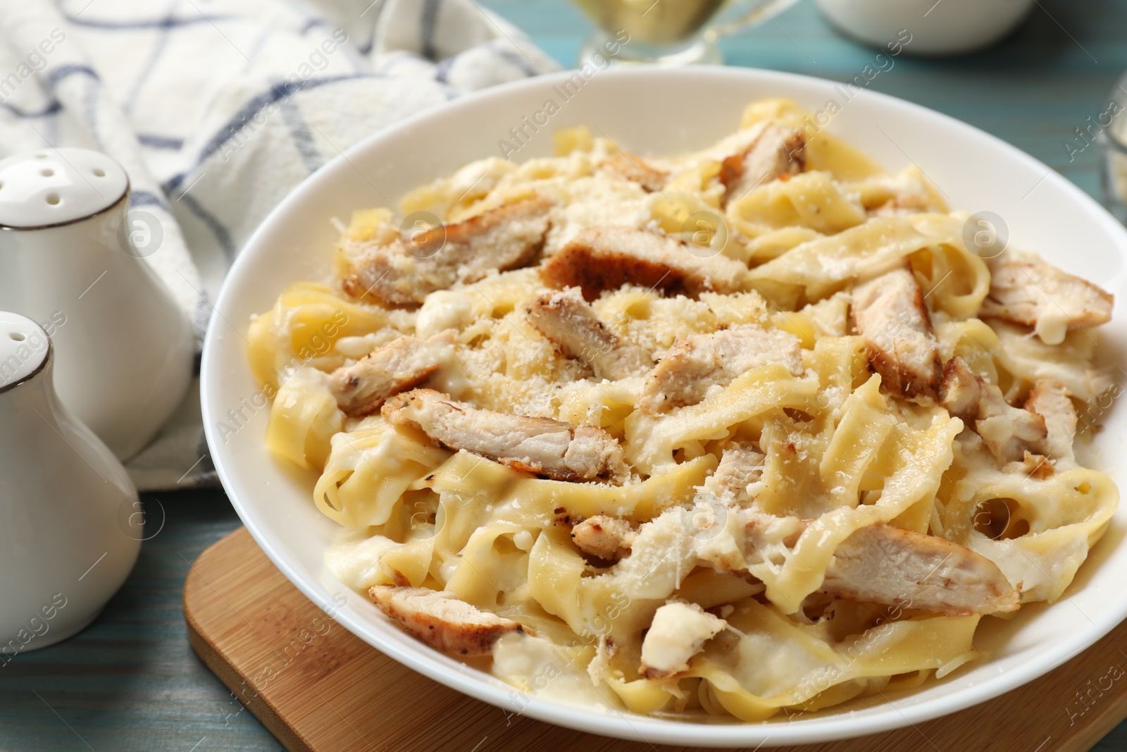 Photo of Tasty Alfredo pasta with chicken on light blue wooden table, closeup