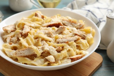 Photo of Tasty Alfredo pasta with chicken on light blue wooden table, closeup