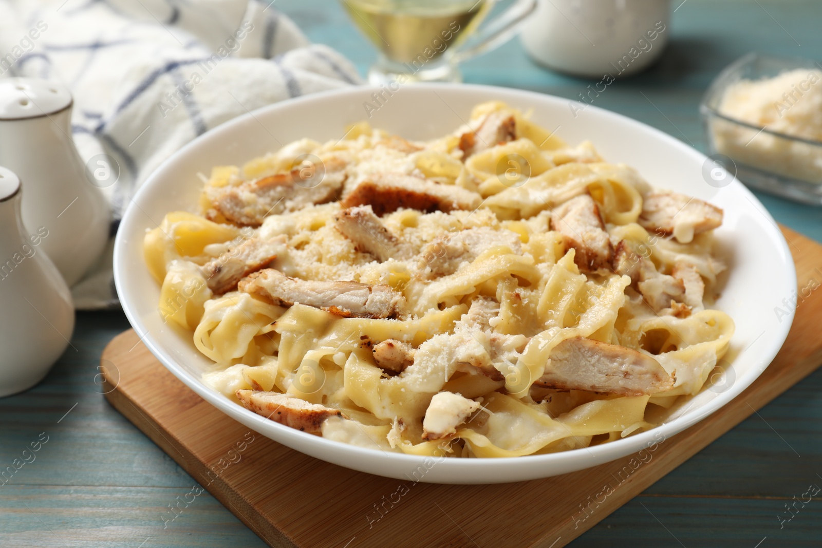 Photo of Tasty Alfredo pasta with chicken on light blue wooden table