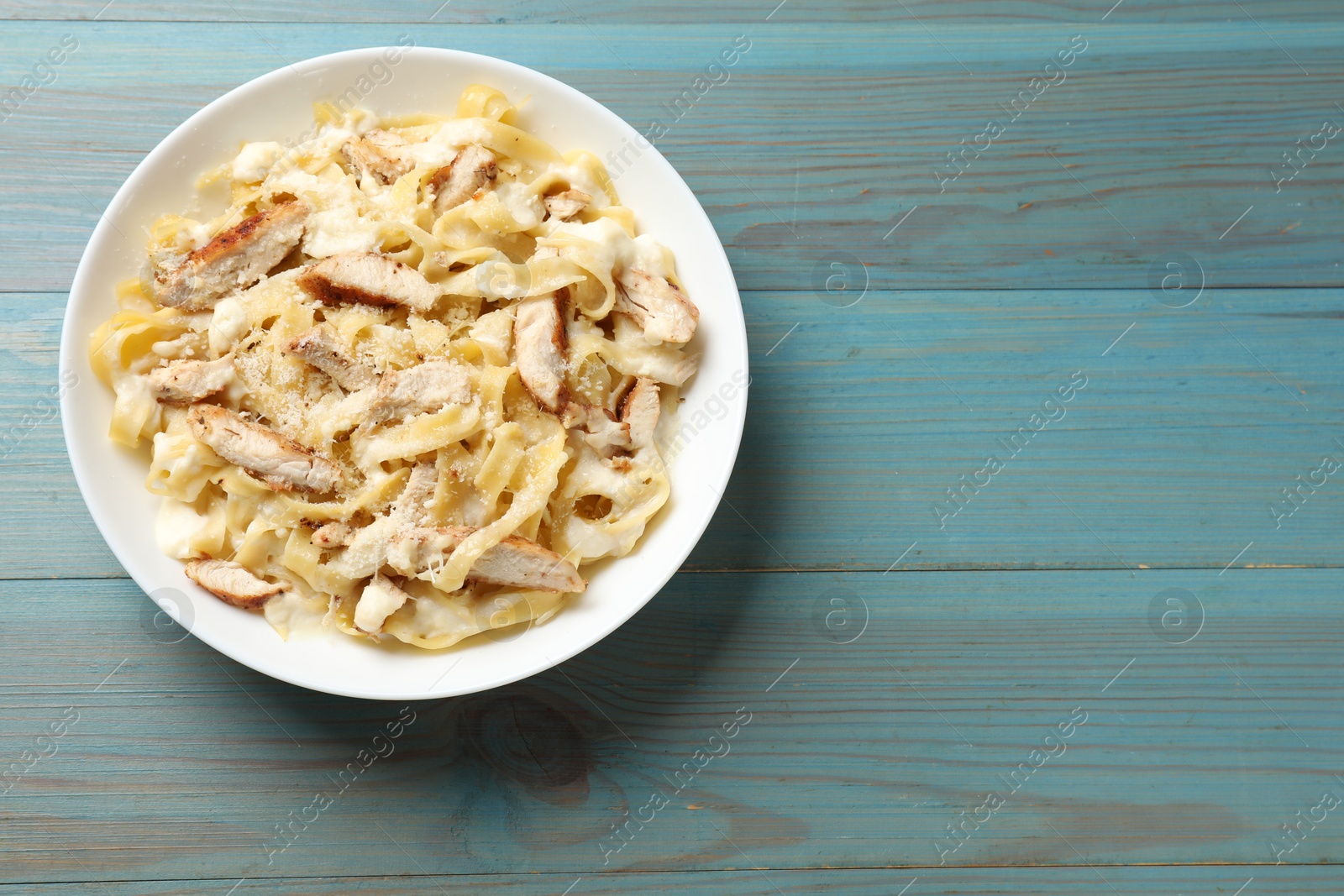 Photo of Tasty Alfredo pasta with chicken on light blue wooden table, top view. Space for text