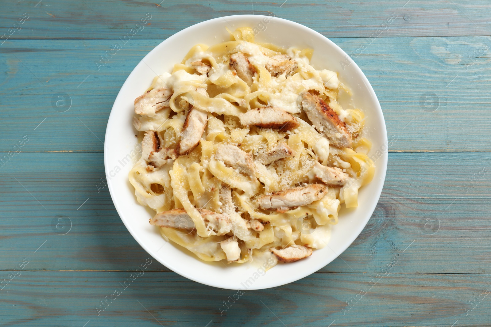 Photo of Tasty Alfredo pasta with chicken on light blue wooden table, top view