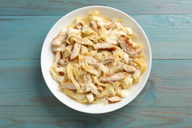 Photo of Tasty Alfredo pasta with chicken on light blue wooden table, top view