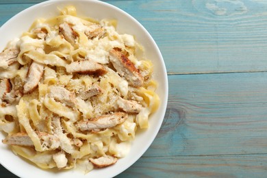 Photo of Tasty Alfredo pasta with chicken on light blue wooden table, top view. Space for text