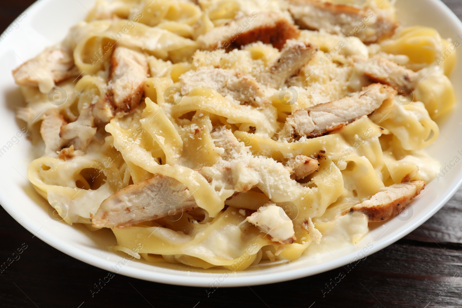 Photo of Tasty Alfredo pasta with chicken on wooden table, closeup