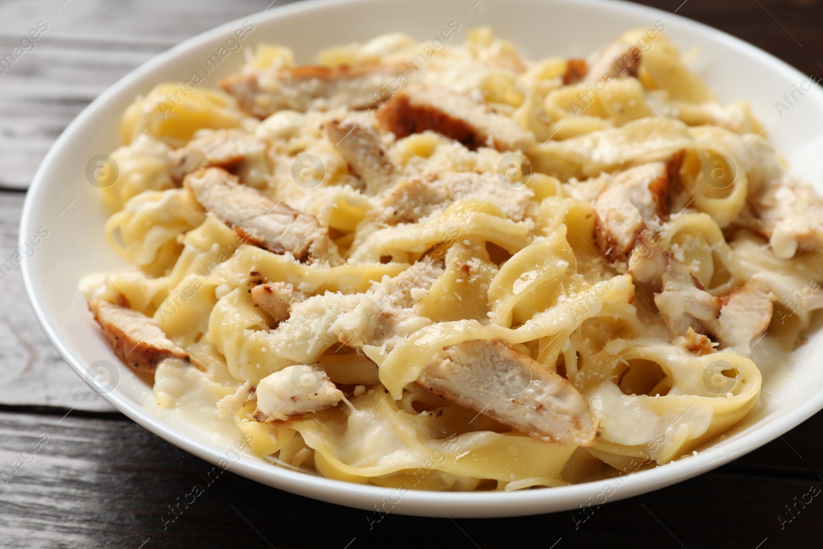 Photo of Tasty Alfredo pasta with chicken on wooden table, closeup