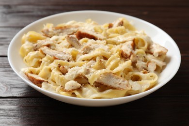 Photo of Tasty Alfredo pasta with chicken on wooden table, closeup