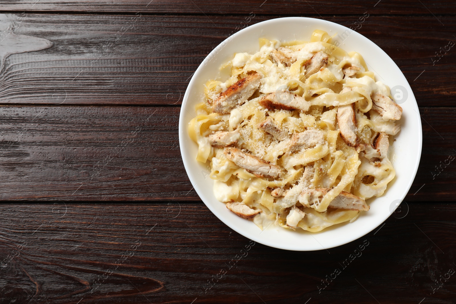 Photo of Tasty Alfredo pasta with chicken on wooden table, top view. Space for text