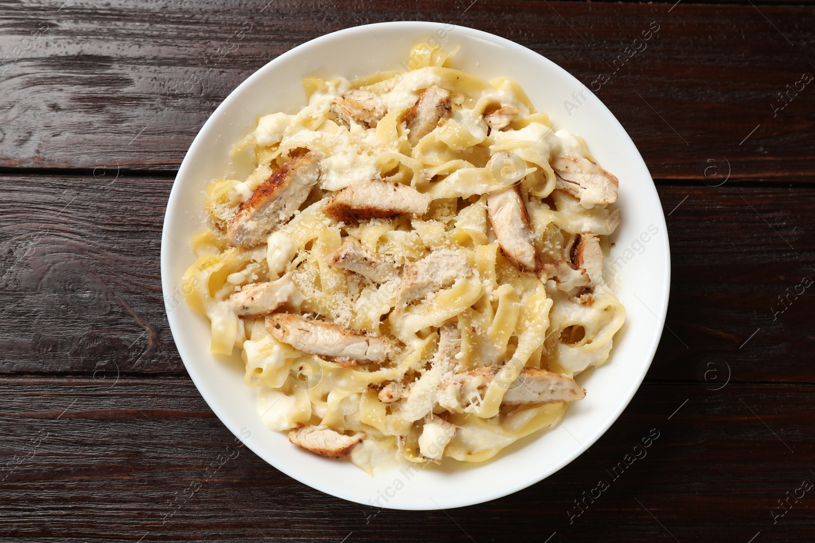 Photo of Tasty Alfredo pasta with chicken on wooden table, top view