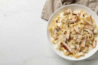 Photo of Tasty Alfredo pasta with chicken on white marble table, top view. Space for text