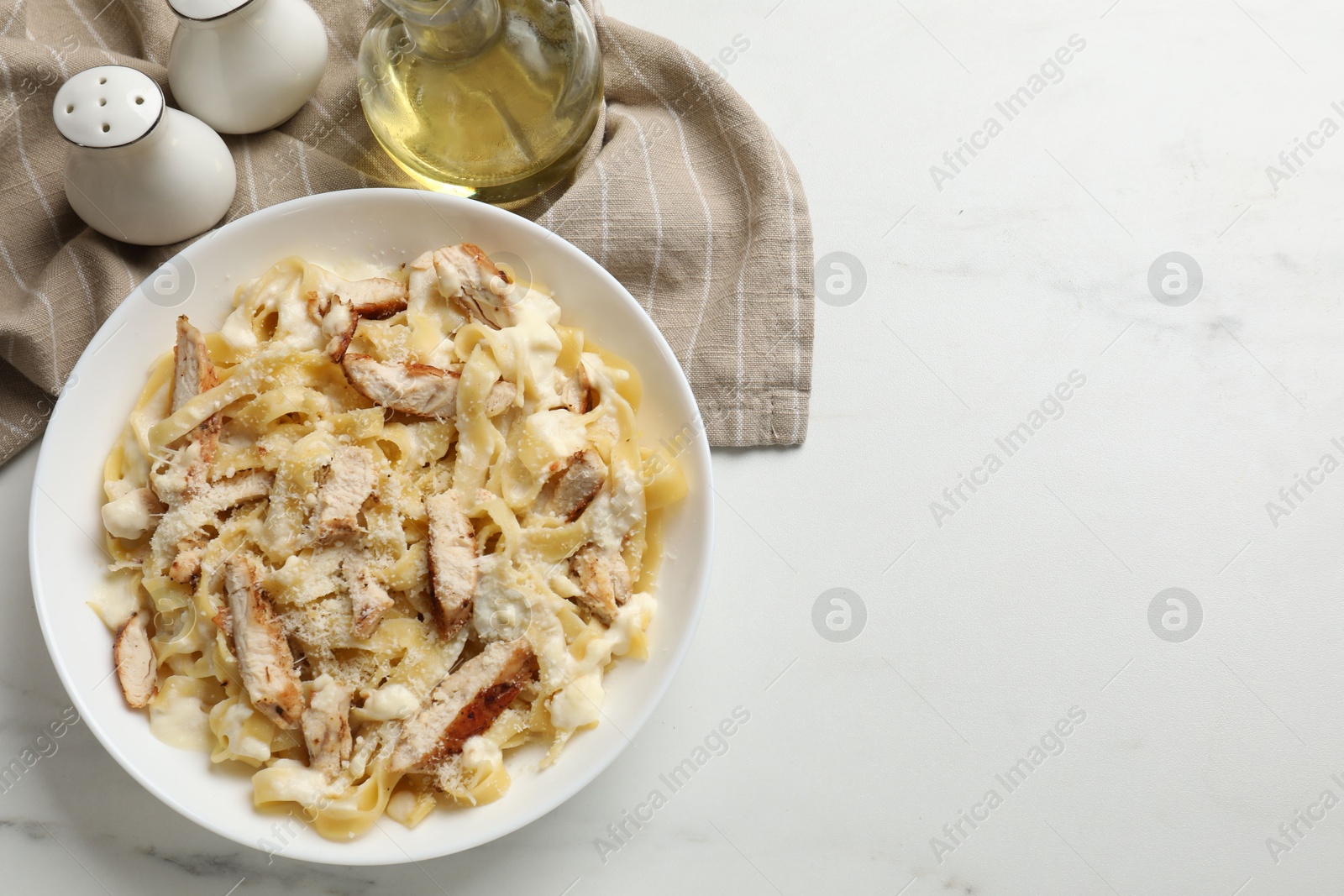 Photo of Tasty Alfredo pasta with chicken on white marble table, flat lay. Space for text