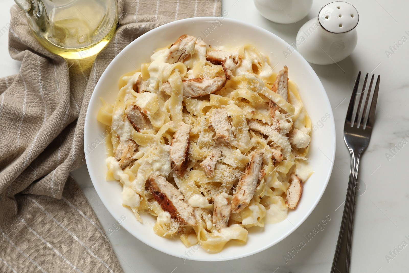 Photo of Tasty Alfredo pasta with chicken served on white marble table, flat lay