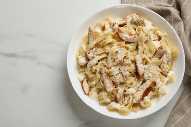 Photo of Tasty Alfredo pasta with chicken on white marble table, top view. Space for text