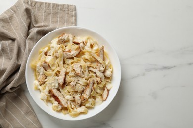 Photo of Tasty Alfredo pasta with chicken on white marble table, top view. Space for text