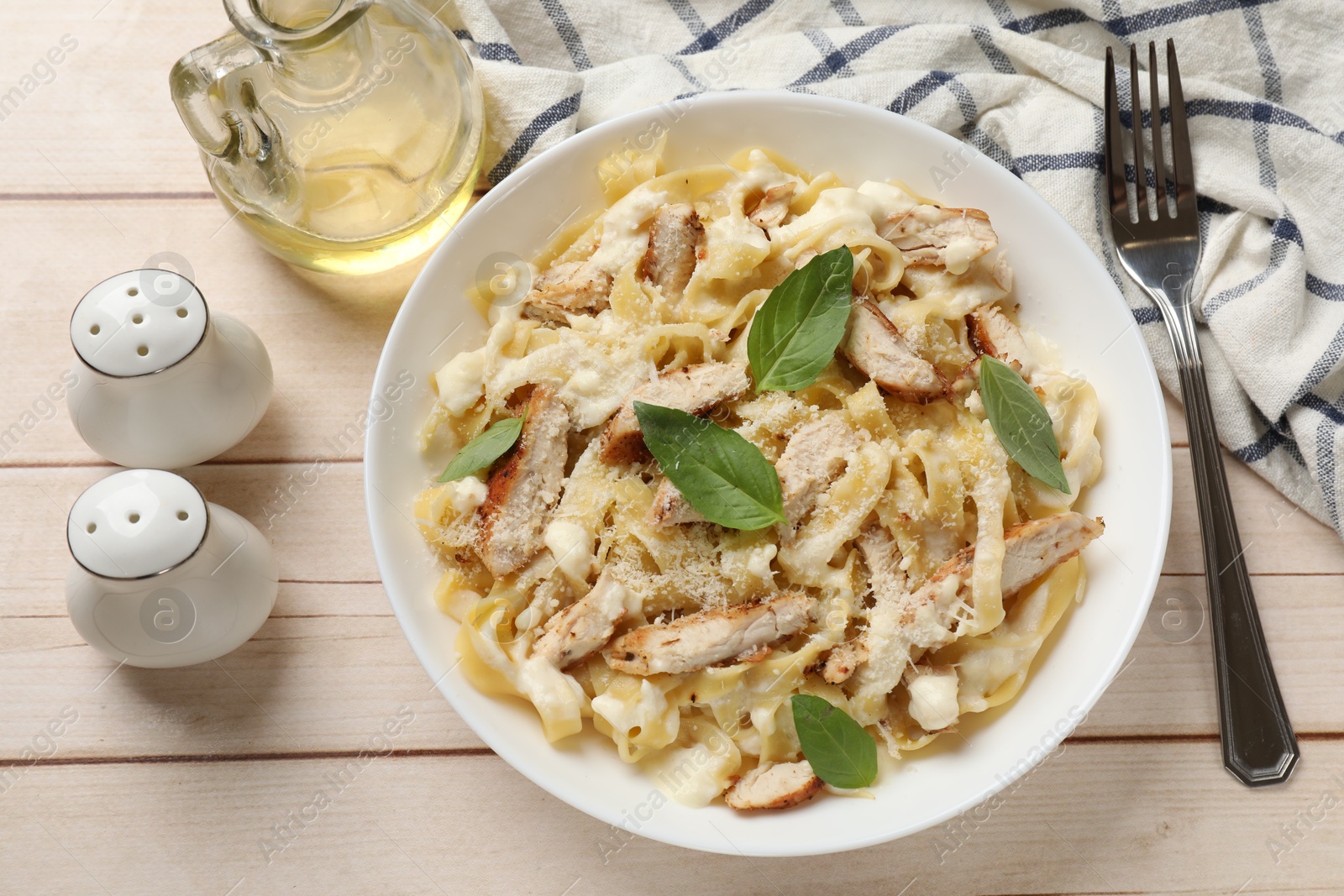 Photo of Tasty Alfredo pasta with chicken served on light wooden table, flat lay