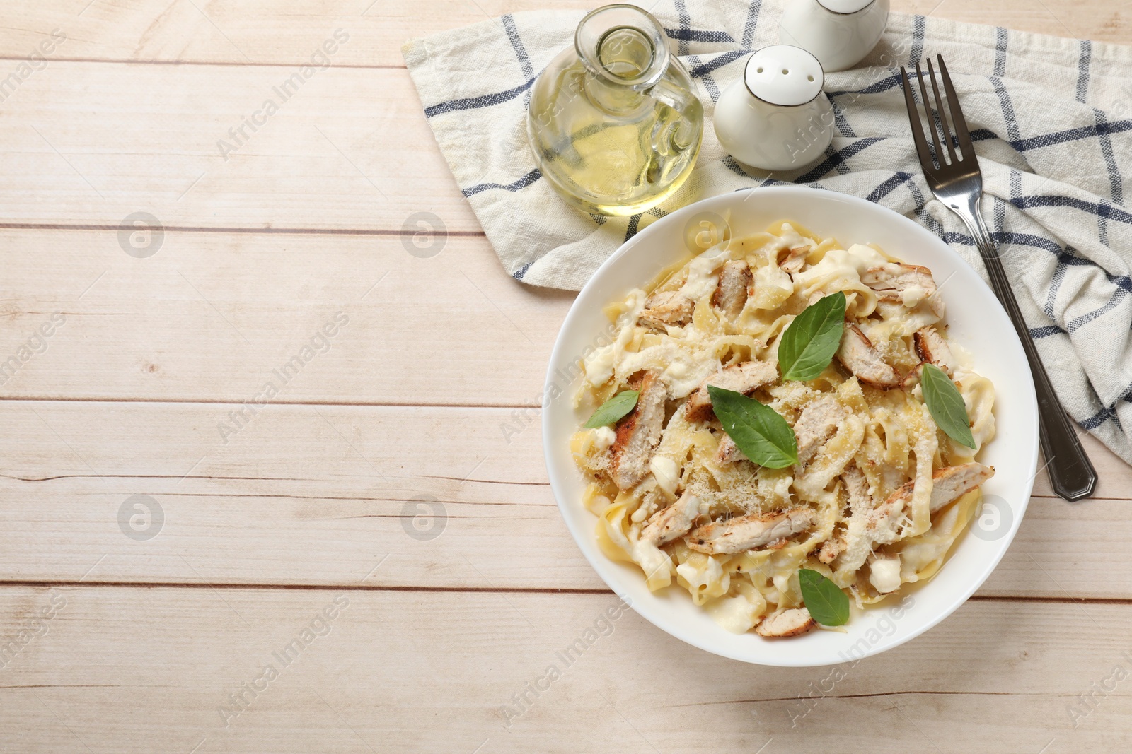 Photo of Tasty Alfredo pasta with chicken served on light wooden table, flat lay. Space for text