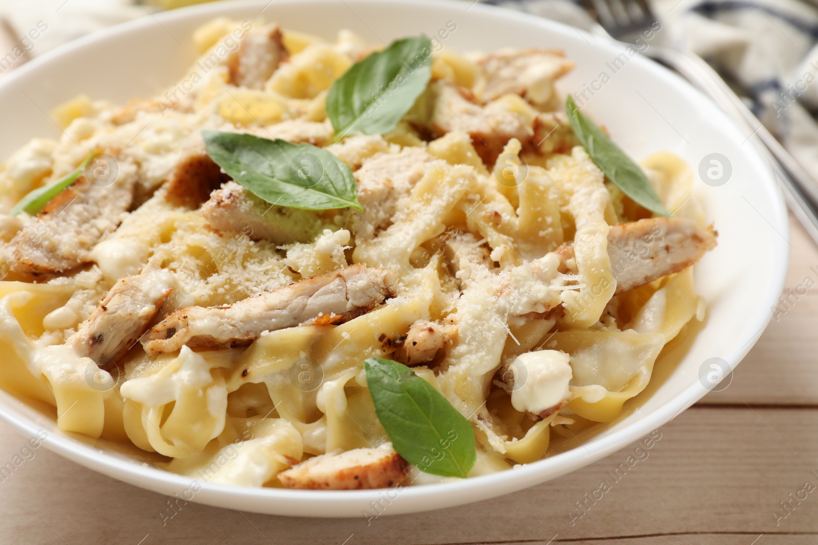 Photo of Tasty Alfredo pasta with chicken on light wooden table, closeup