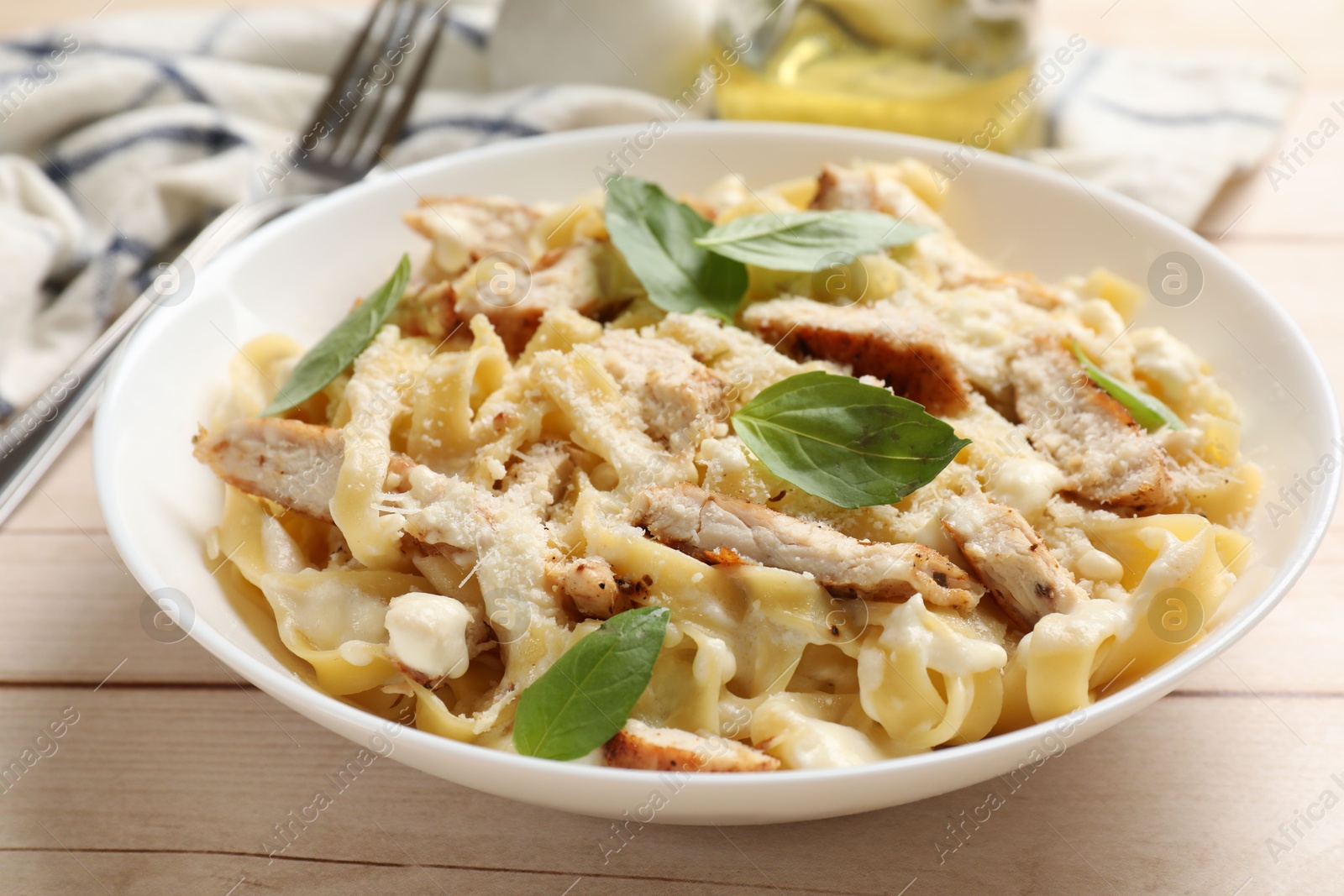 Photo of Tasty Alfredo pasta with chicken on light wooden table