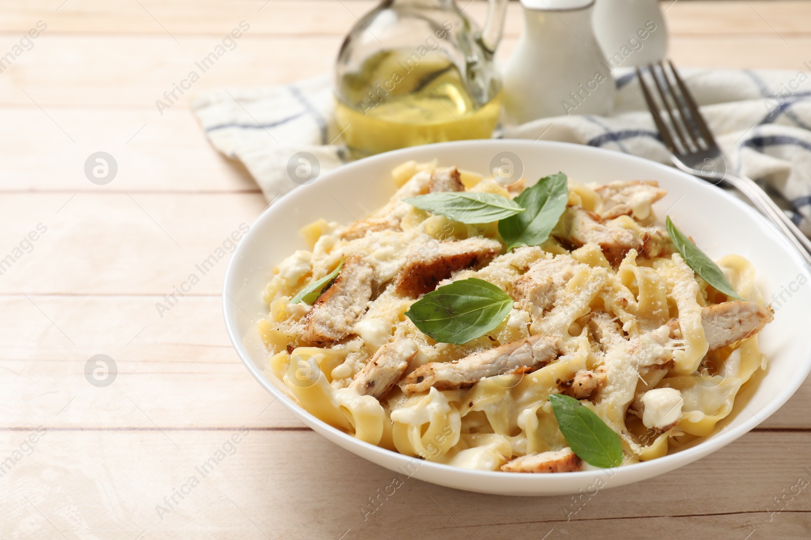 Photo of Tasty Alfredo pasta with chicken on light wooden table, space for text