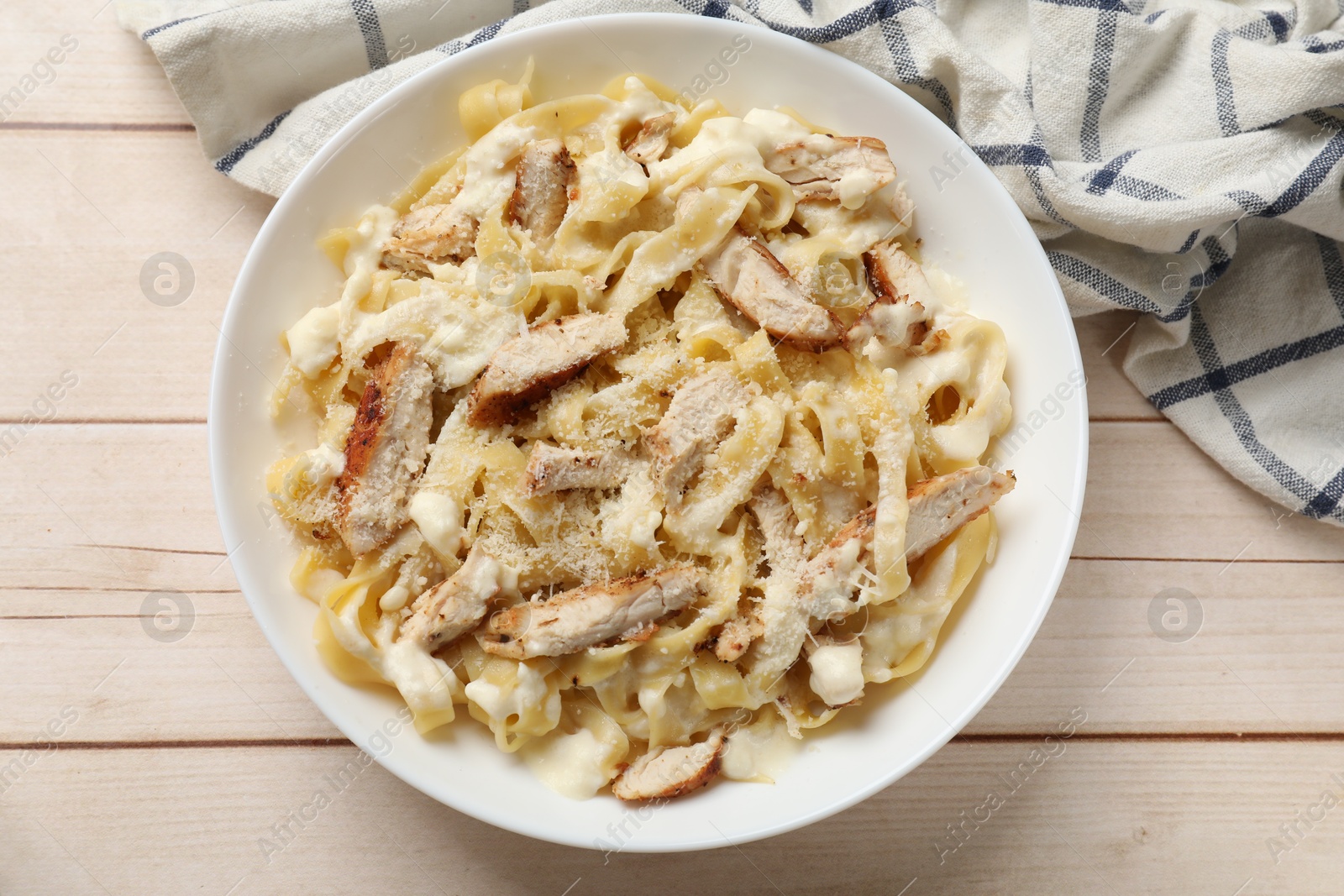 Photo of Tasty Alfredo pasta with chicken on light wooden table, top view