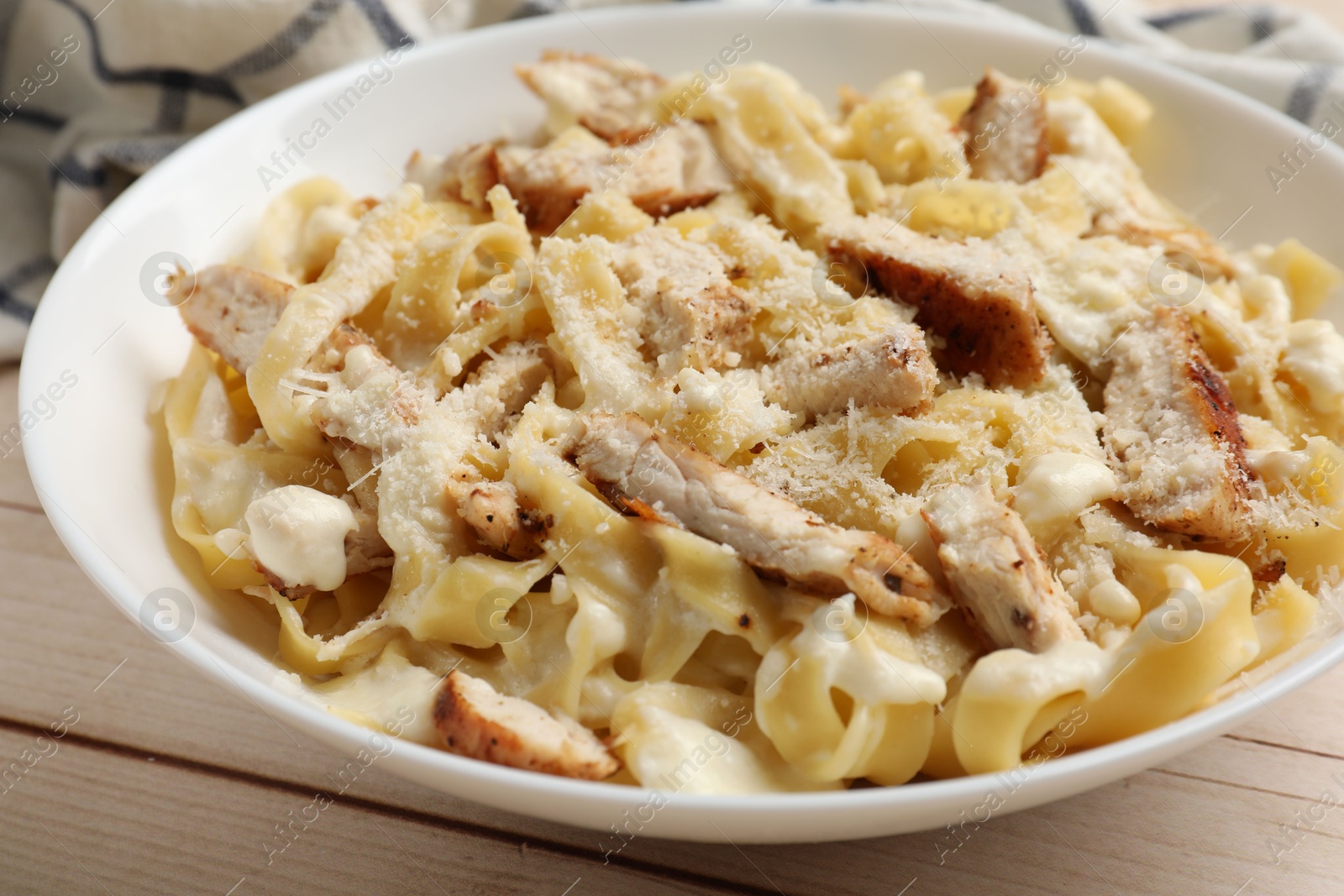 Photo of Tasty Alfredo pasta with chicken on light wooden table, closeup