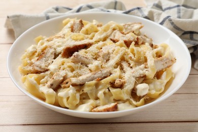 Photo of Tasty Alfredo pasta with chicken on light wooden table, closeup